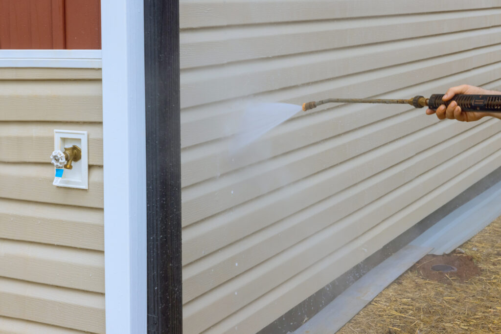 Service worker expertly handles high pressure nozzles to spray water and soap cleaner on siding houses during cleaning process.